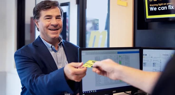 An auto technician handing a customer their Meineke Credit Card